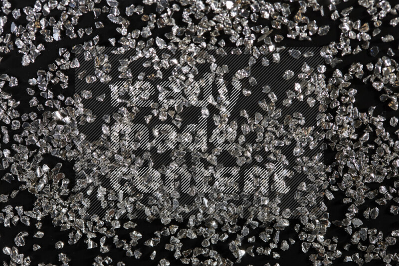 Silver shimmering fragments of glass scattered on a black background