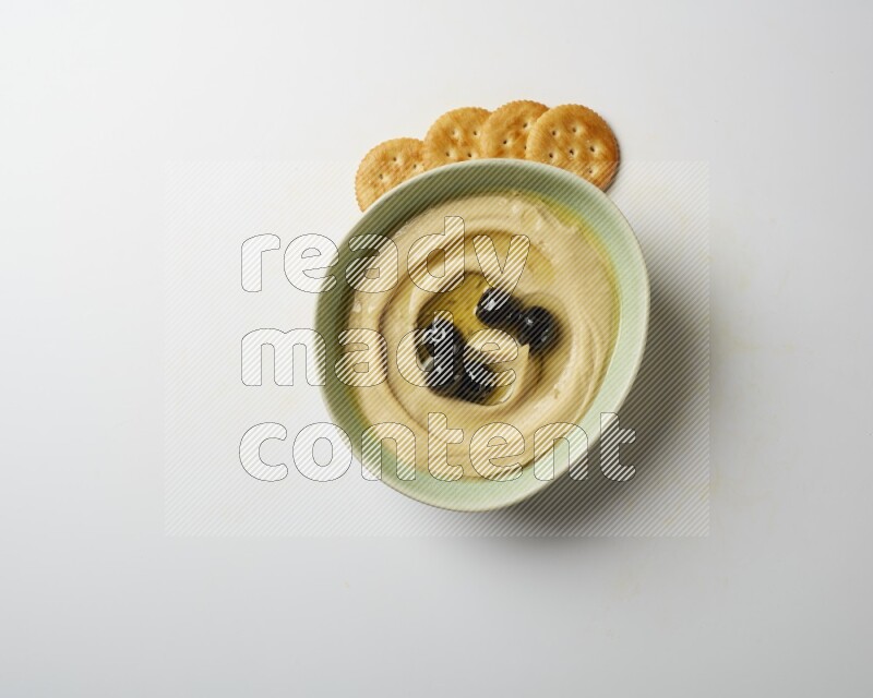 Hummus in a green plate garnished with black olives on a white background