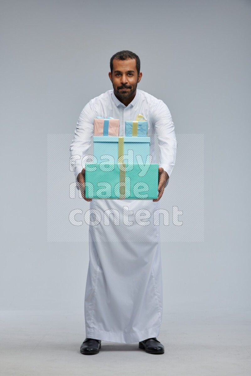 Saudi man Wearing thob standing holding gift box on Gray background