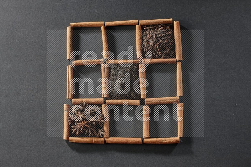 9 squares of cinnamon sticks full of tea in the middle surrounded by nutmeg, dried mint, cloves, dried basil, dried ginger, cinnamon, star anise and cardamom on black flooring