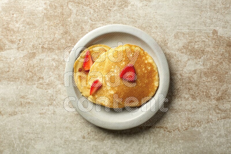 Three stacked strawberry pancakes in a grey plate on beige background