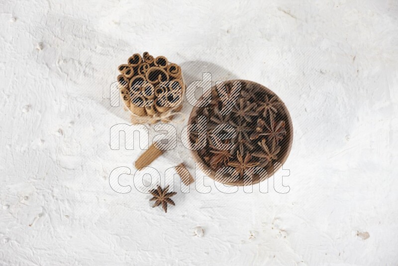 A stacked and bounded cinnamon sticks and a wooden bowl full of star anise on a white background