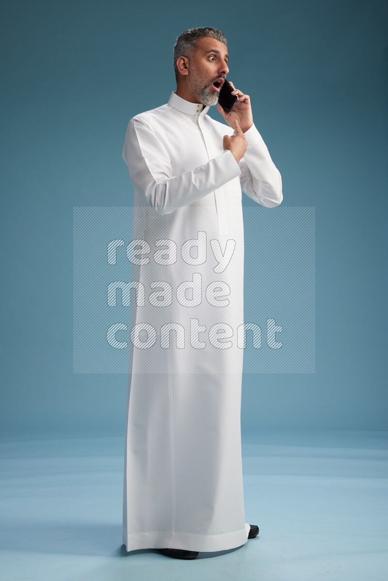 Saudi man wearing thob talking on the phone on blue background