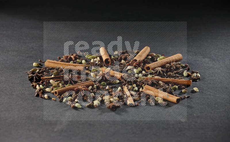 Cardamom, star anise, cloves and cinnamon sticks on black flooring