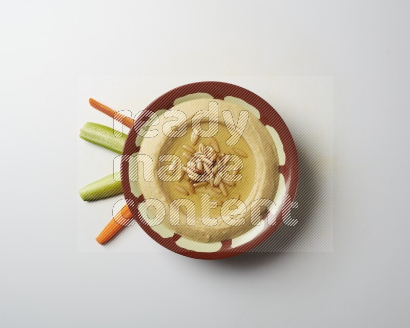 Hummus in a traditional plate garnished with pine nuts on a white background
