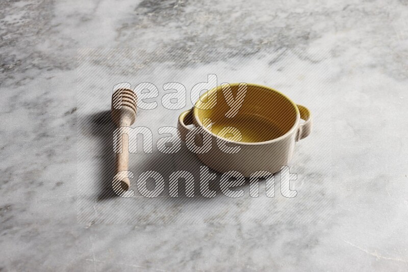 Multicolored pottery bowl with wooden honey dipper on the side on grey marble background