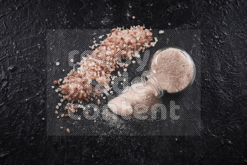 A glass jar full of fine himalayan salt with some himalayan crystals beside it on a black background
