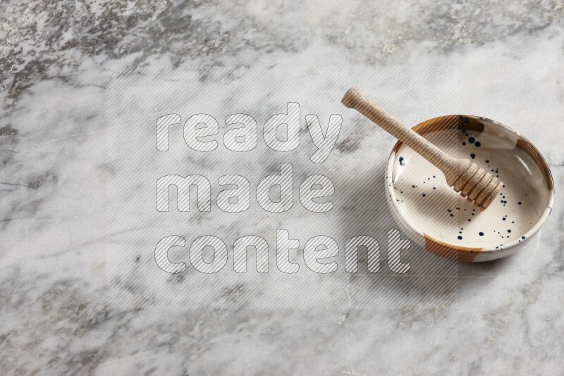 Multicolored pottery bowl with wooden honey dipper in it on grey marble background