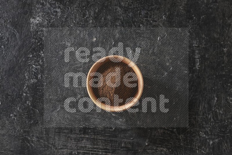 A wooden bowl full of cloves powder on a textured black flooring