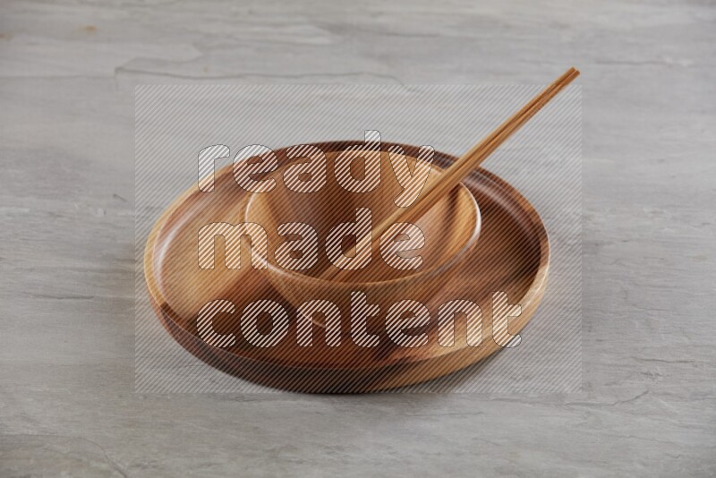 brown wood round bowl on top of brown wood round plate and wood chopsticks, on grey textured countertop