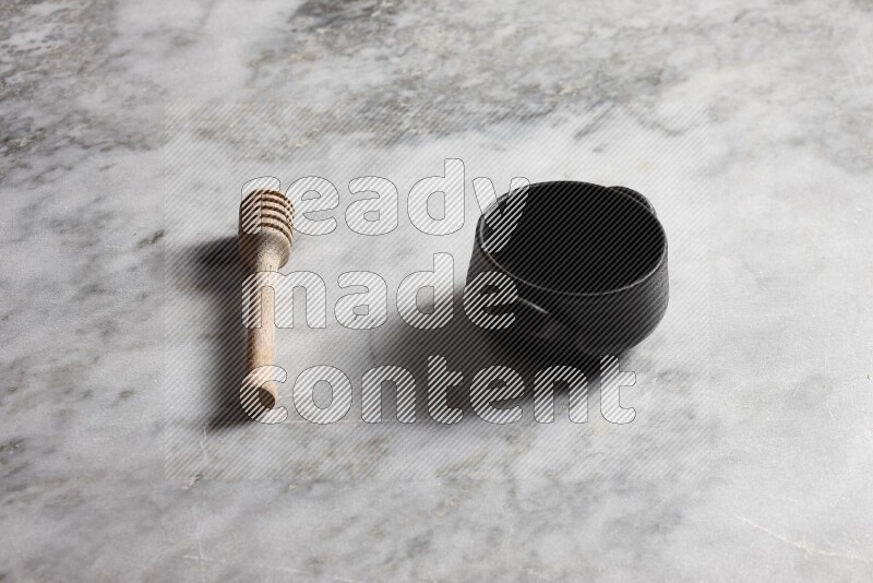 Black pottery bowl with wooden honey dipper on the side on grey marble background