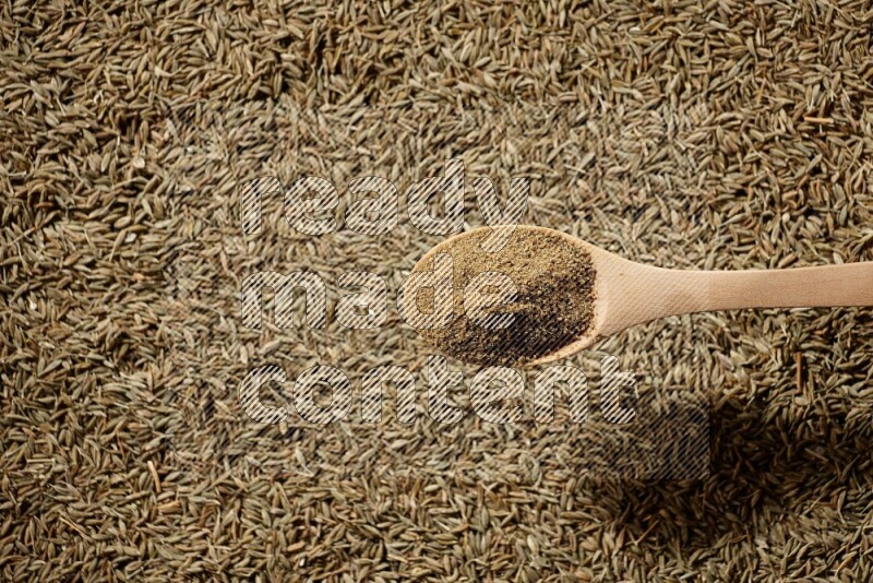 A wooden spoon full of cumin powder on a cumin seeds background