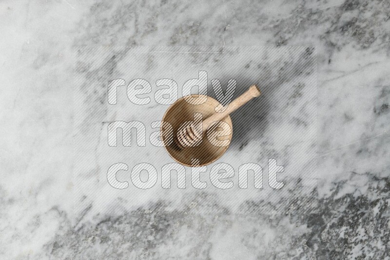 Beige pottery bowl with wooden honey dipper in it on grey marble background