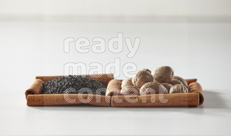 مربعان من أعواد القرفة ممتلئان بحبة البركة السوداء وجوزة الطيب علي خلفية بيضاء