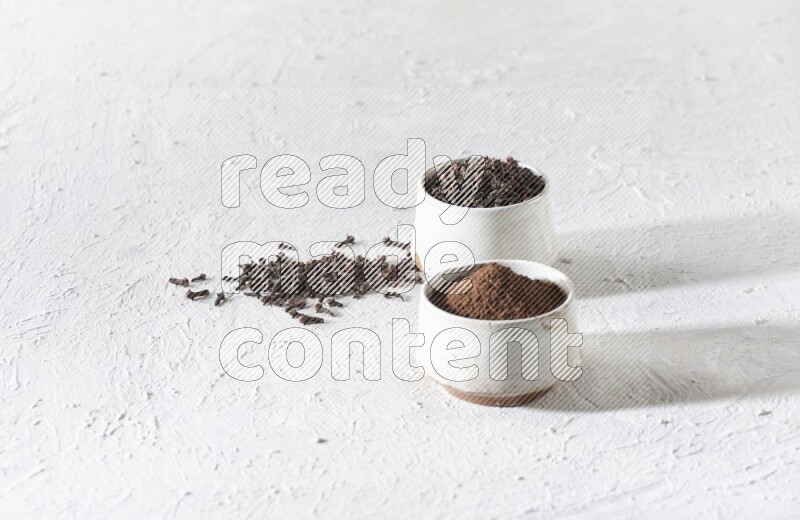 2 Beige ceramic bowls, one full of cloves and the other full of powder on textured white flooring