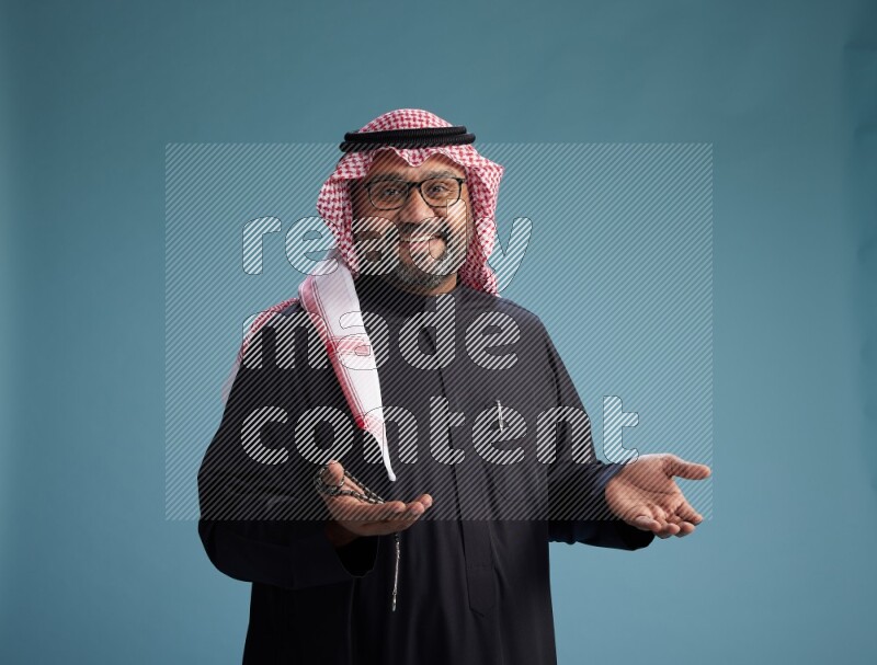 Saudi Man with shimag Standing Interacting with the camera on blue background