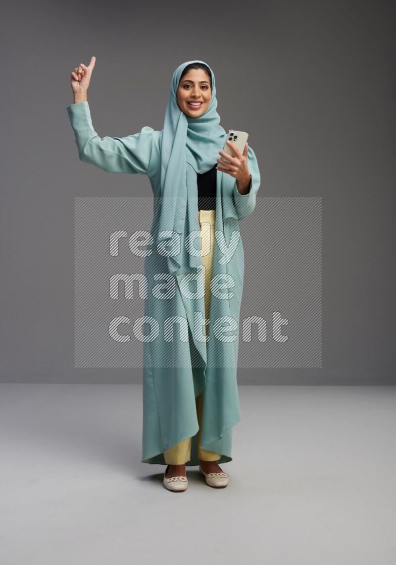 Saudi Woman wearing Abaya standing texting on phone on Gray background