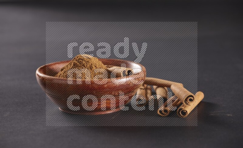 Cinnamon powder in a wooden bowl with a cinnamon sticks on black background