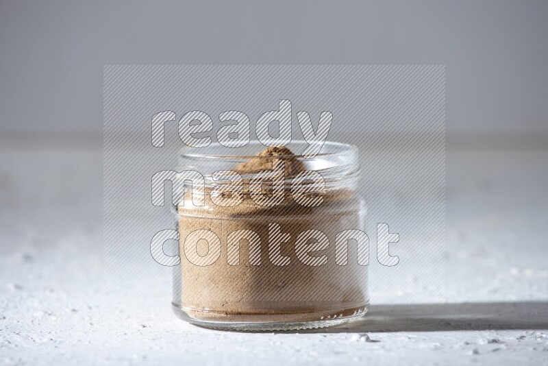 A glass jar full of allspice powder on a textured white flooring