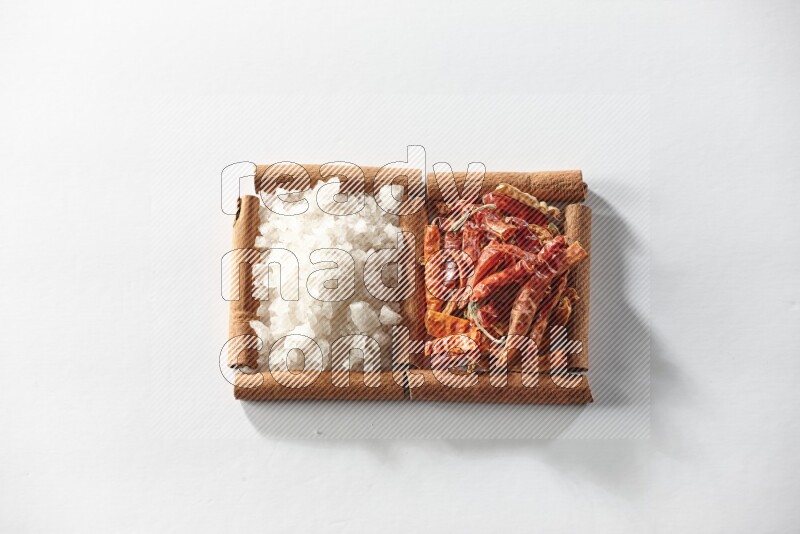 2 squares of cinnamon sticks full of dried red chilis and white salt on white flooring