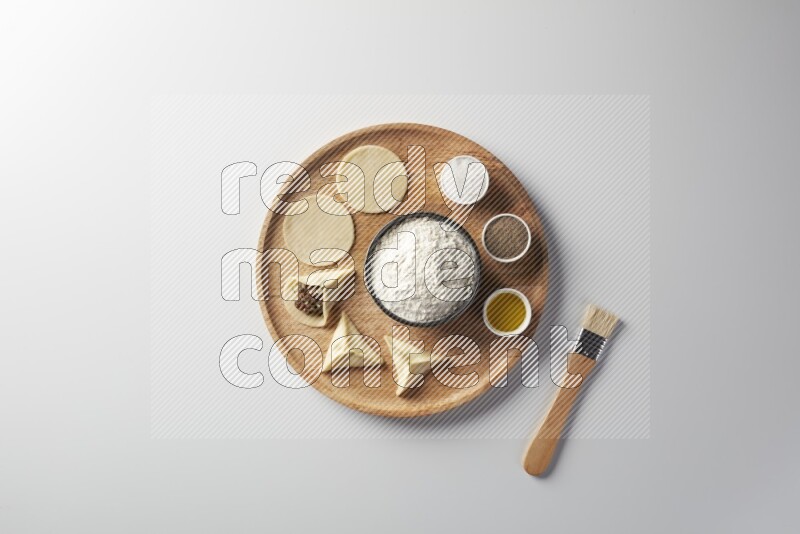 two closed sambosas and one open sambosa filled with meat while flour, salt, black pepper and oil with oil brush aside in a wooden dish on a white background