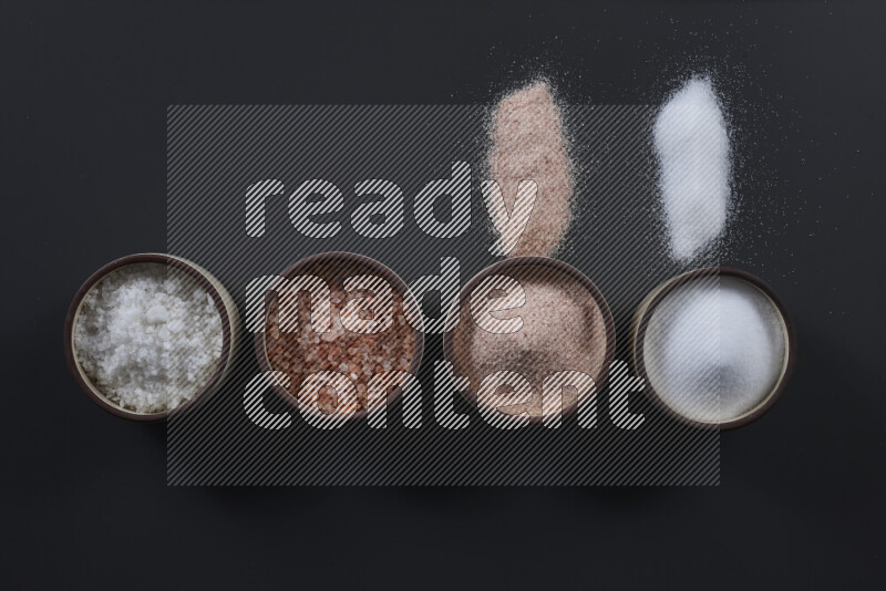 4 pottery bowls filled with himalayan salt and white salt on black background