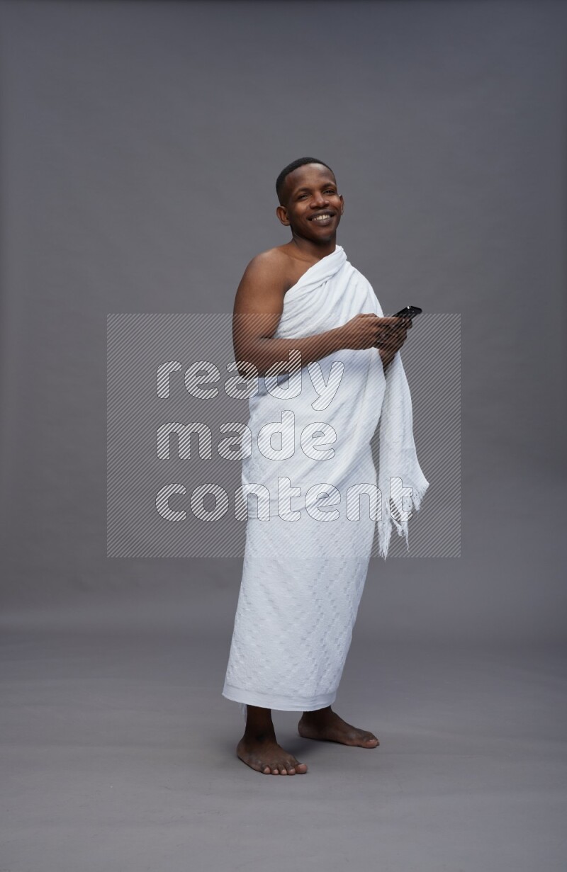 A man wearing Ehram Standing texting on phone on gray background