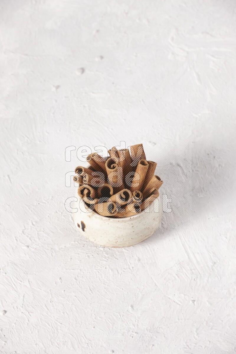 Cinnamon sticks in a beige bowl on a white background