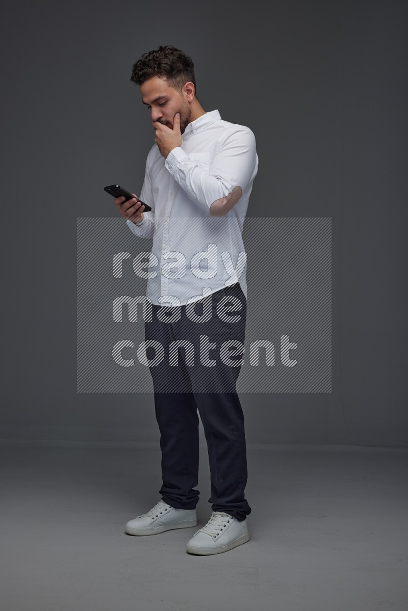 A man wearing smart casual standing and using his phone eye level on a gray background