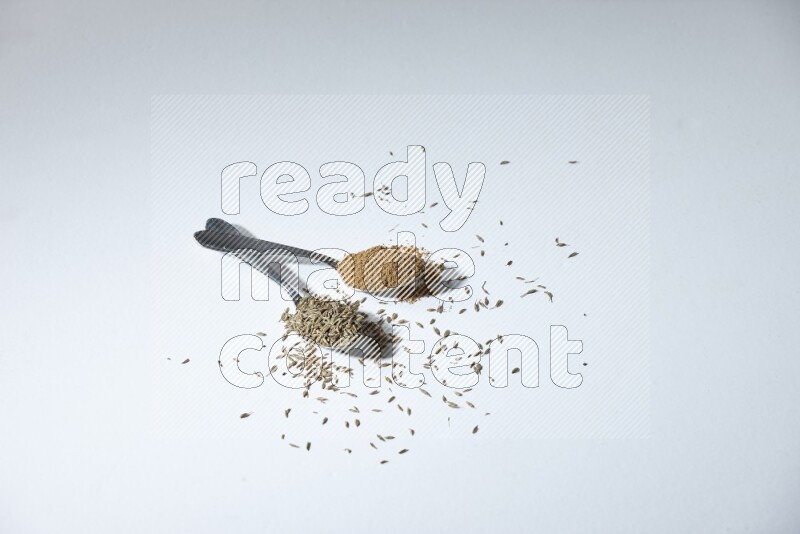 2 metal spoons full of cumin seeds and powder on white flooring