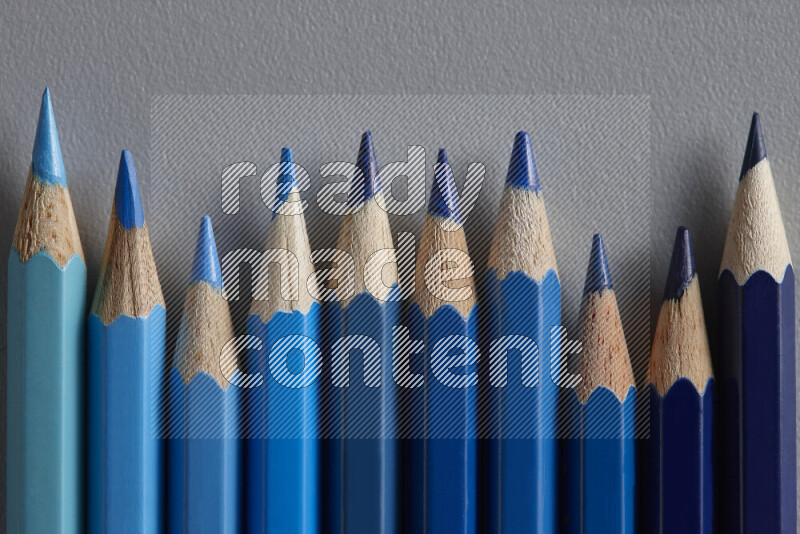 A collection of colored pencils arranged showcasing a gradient of blue hues on grey background
