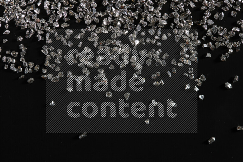 Silver shimmering fragments of glass scattered on a black background