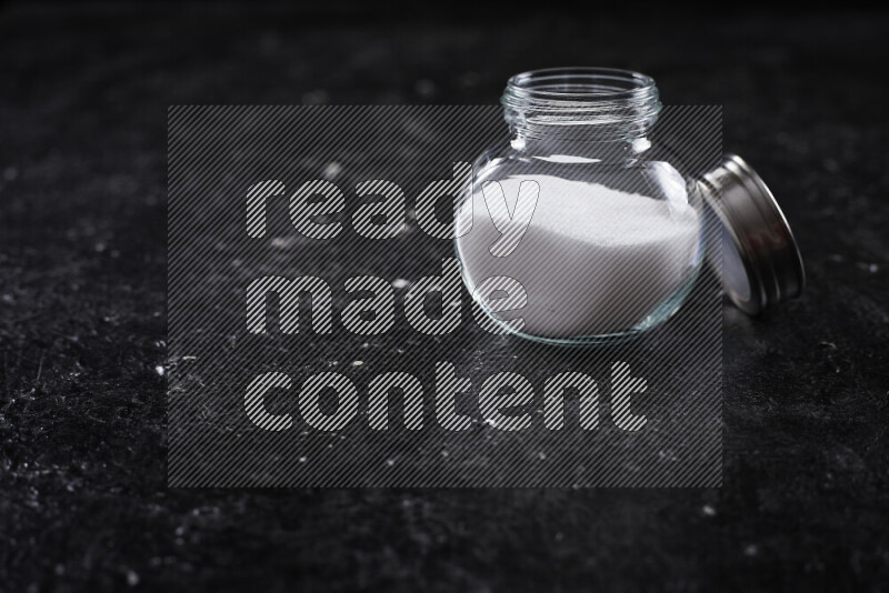 A glass jar full of fine table salt on black background
