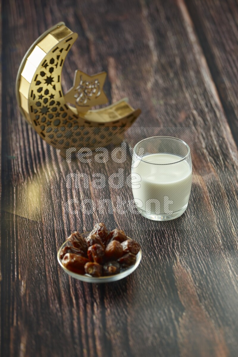 A wooden golden crescent lantern with different drinks, dates, nuts, prayer beads and quran on brown wooden background