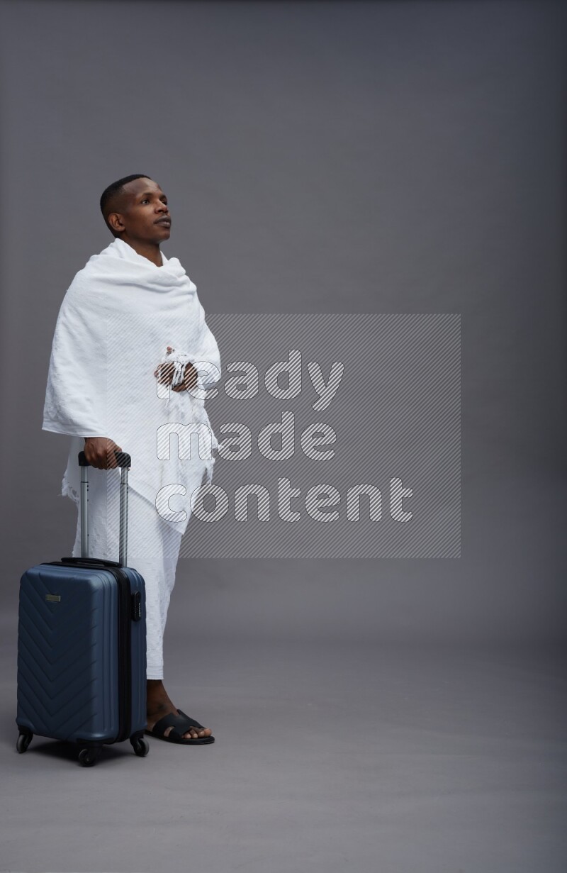 A man wearing Ehram Standing holding traveling bag on gray background