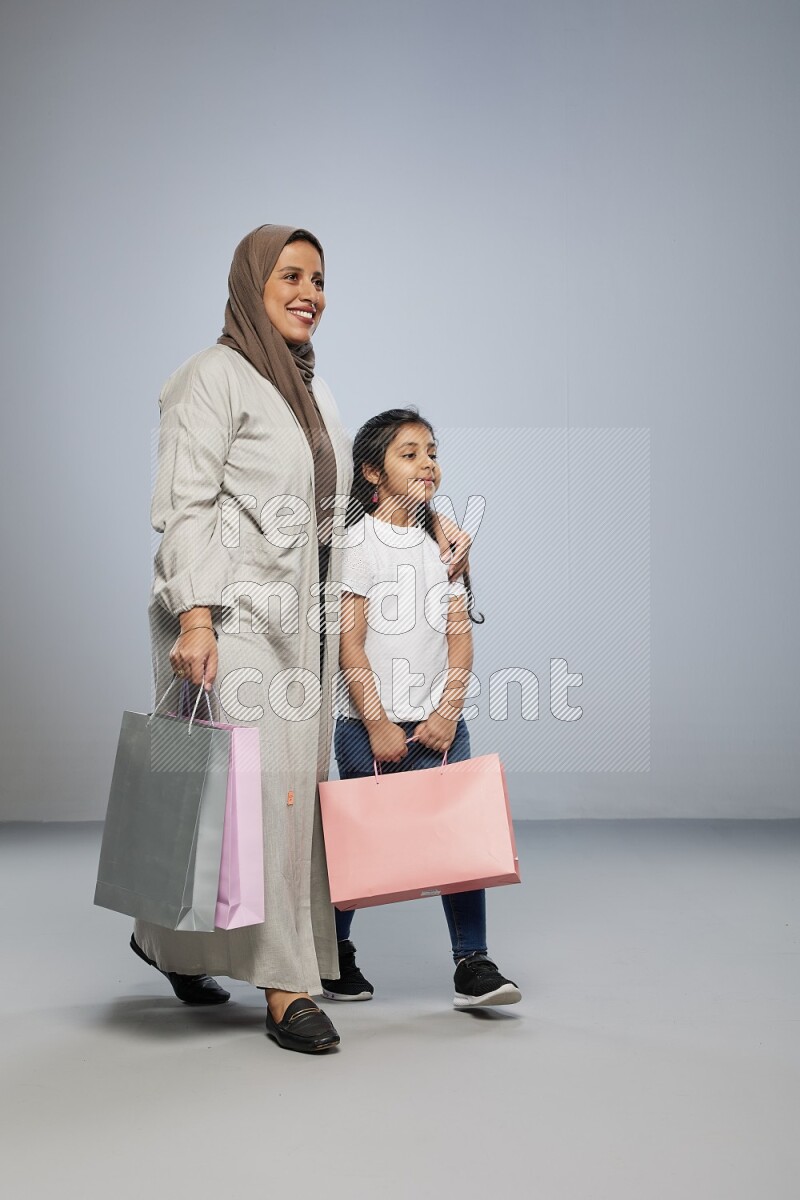 Mom and daughter holding shopping bags on gray background