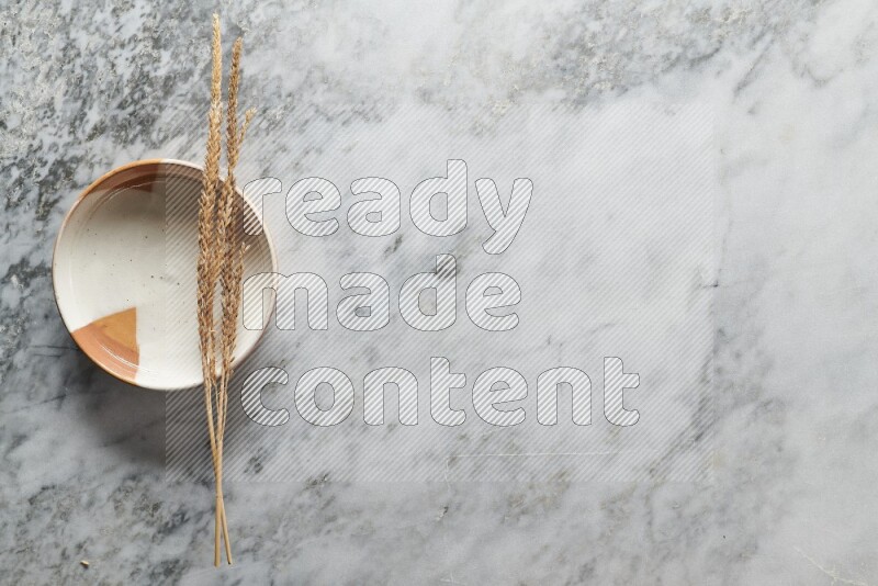 Wheat stalks on multicolored pottery plate on grey marble background