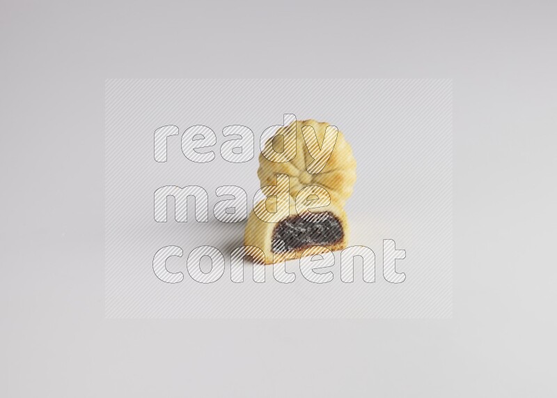 Two Pieces of Maamoul filled with date one of them is cut direct on white background
