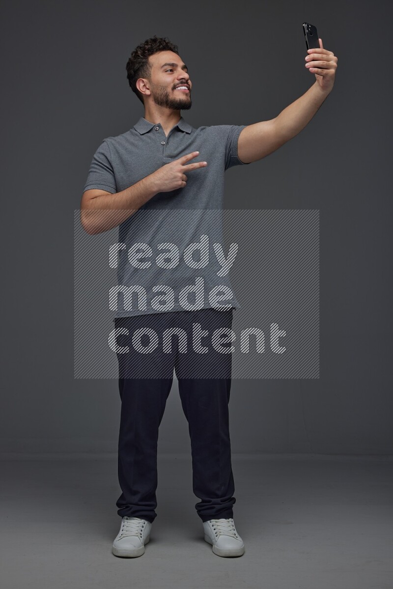 A man wearing casual and taking selfie with his phone different angles eye level on a gray background