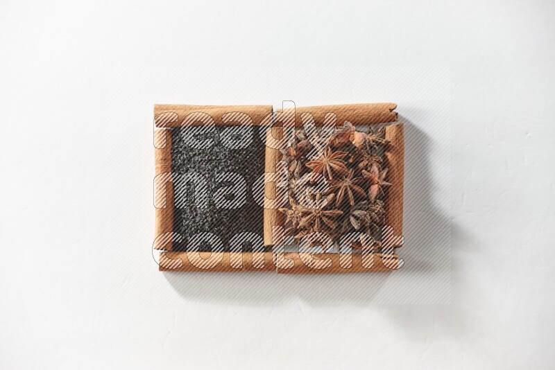 مربعان من أعواد القرفة ممتلئان بحبة البركة السوداء واليانسون النجمي علي خلفية بيضاء