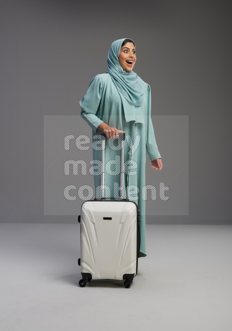 Saudi Woman wearing Abaya standing holding Travel bag on Gray background