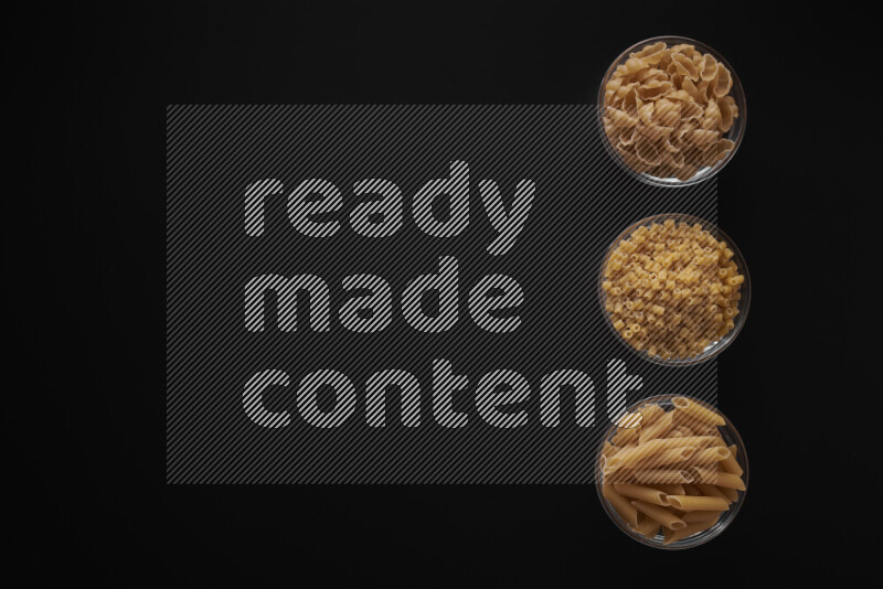 Different pasta types in 3 glass bowls on black background