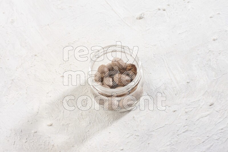 A glass jar full of whole nutmeg seeds on a white flooring
