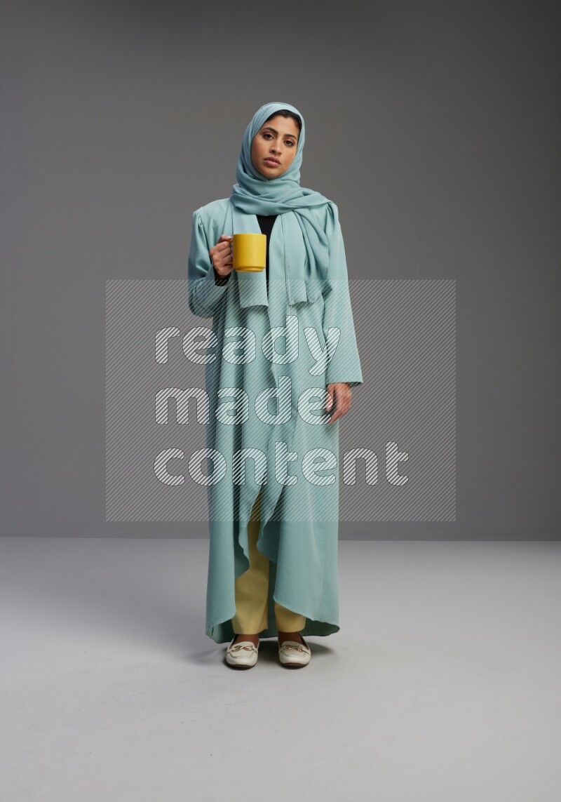 Saudi Woman wearing Abaya standing  holding a mug on Gray background