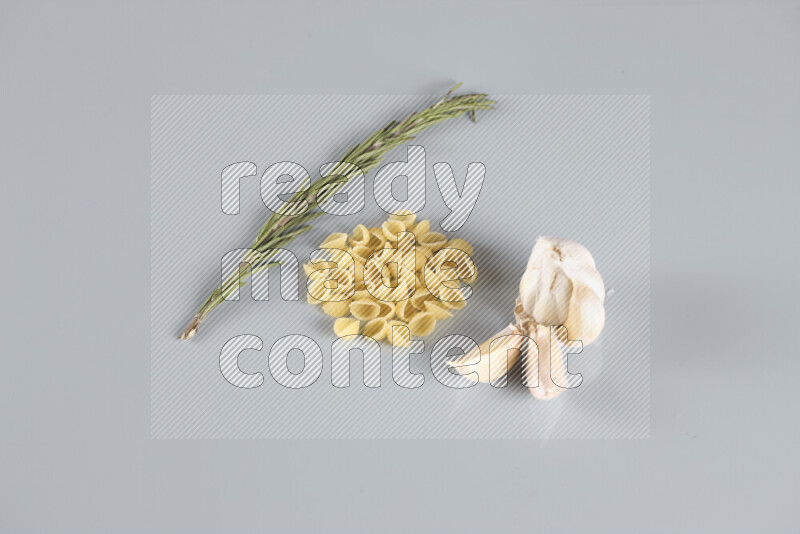 Raw pasta with different ingredients such as cherry tomatoes, garlic, onions, red chilis, black pepper, white pepper, bay laurel leaves, rosemary, cardamom and mushrooms on light blue background