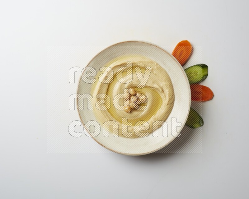 Hummus in a pottry plate garnished with roasted chickpeas on a white background