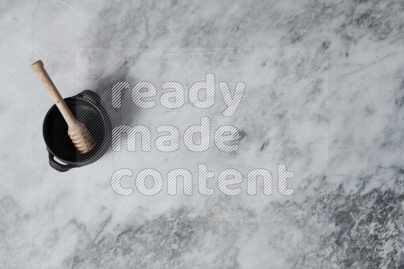 Black pottery bowl with wooden honey dipper in it on grey marble background