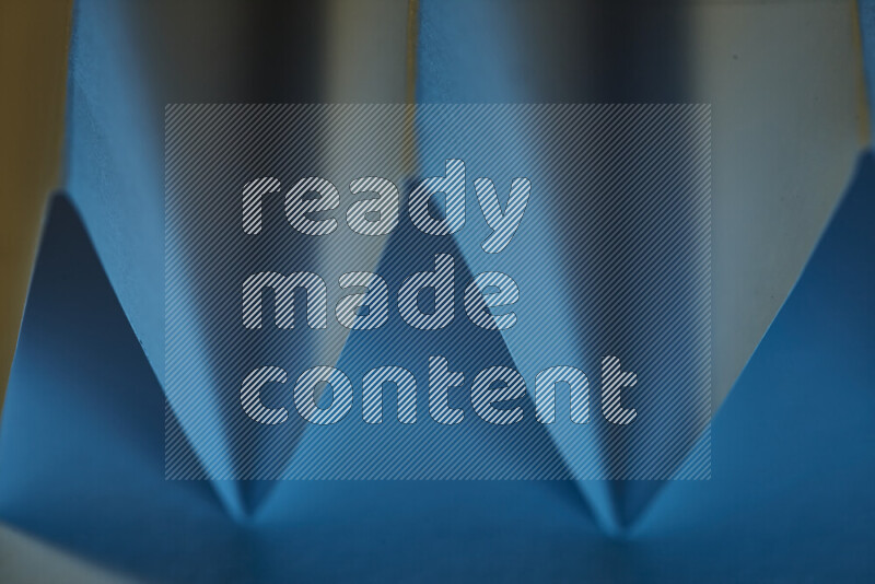 صورة مجردة مقربة تظهر طيات ورقية هندسية حادة بتدرجات اللون الأزرق مع درجات لونية دافئة