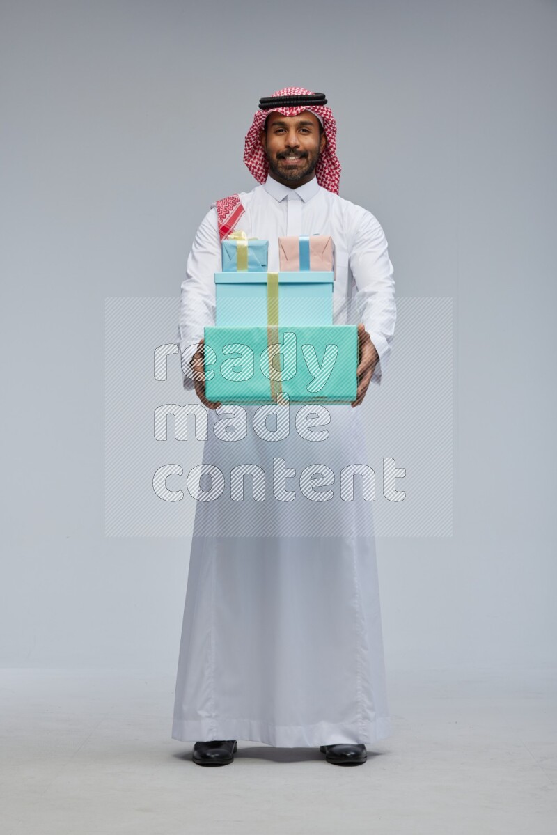 Saudi man Wearing Thob and shomag standing holding gift box on Gray background