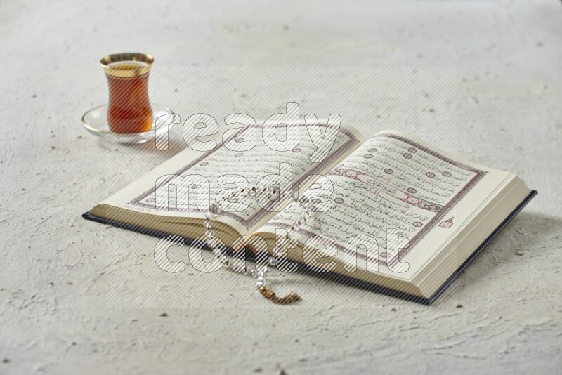 Quran with dates, prayer beads and different drinks all placed on textured white background